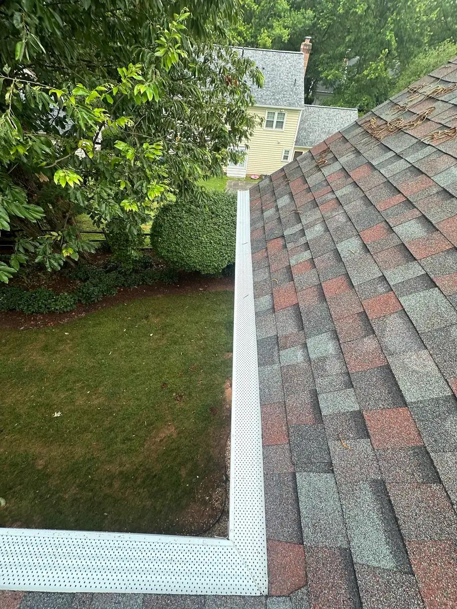 A white perforated gutter guard running along a shingled roof edge above a lawn