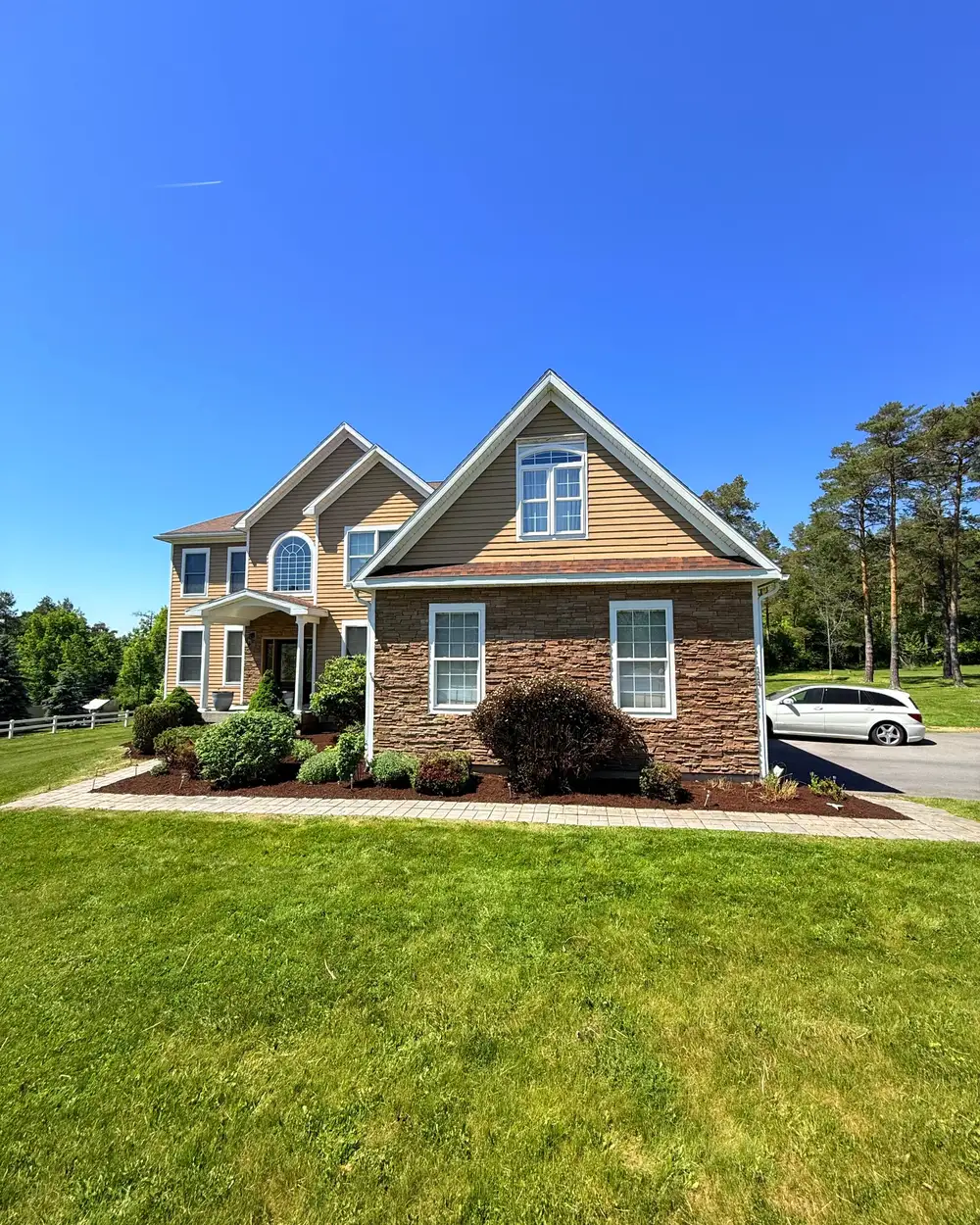 A mown lawn, clipped shrubs and mulched beds across the front of a house