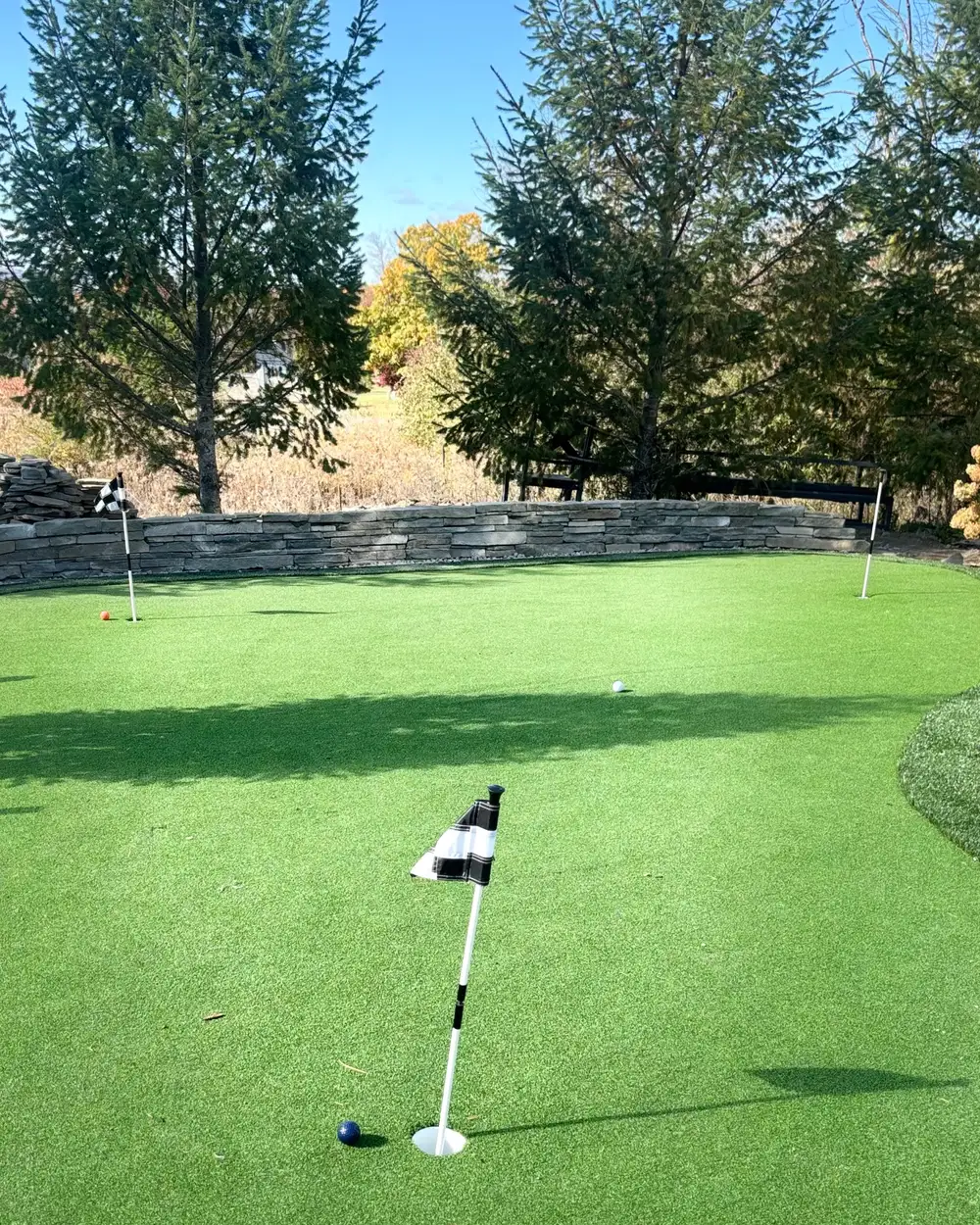 A synthetic-turf putting green above a stacked stone wall