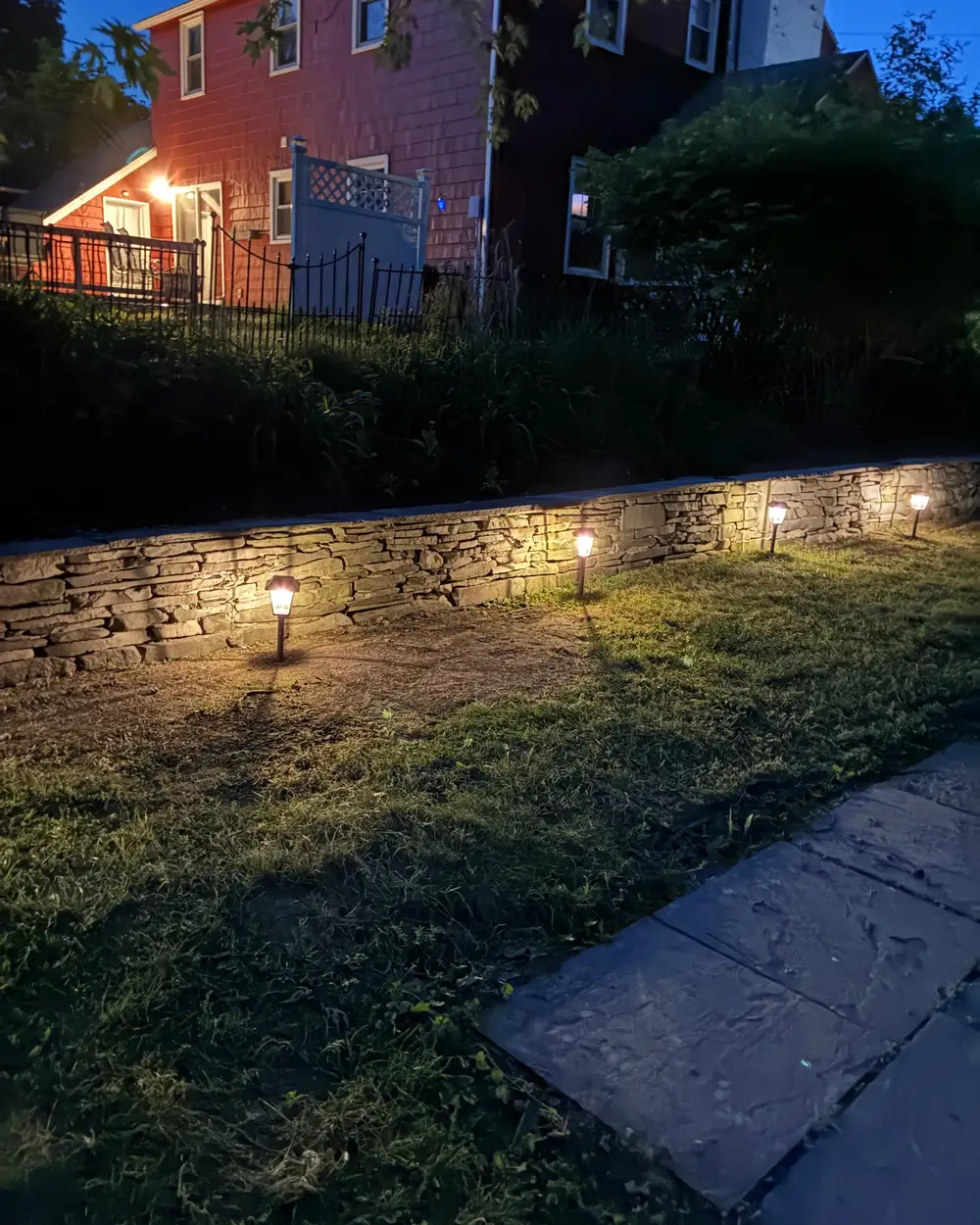 A dry-stacked stone retaining wall lit by path lights at dusk on an Ithaca property