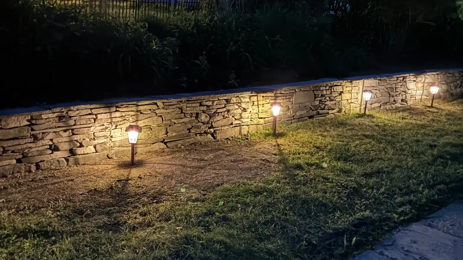A dry-stacked stone retaining wall lit by path lights at dusk on an Ithaca property